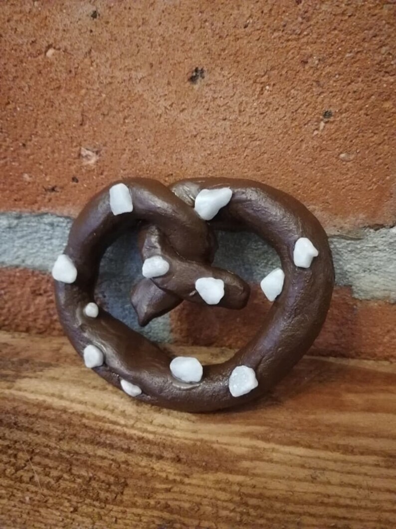 May include: A brown pretzel with white sugar crystals on top. The pretzel is on a wooden surface.