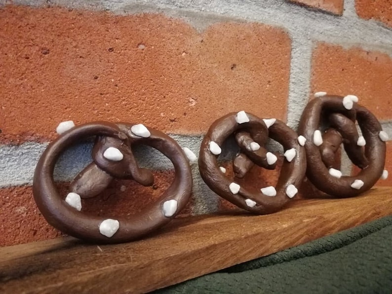 May include: Three brown pretzel shaped ornaments with white decorative accents. The ornaments are arranged on a wooden surface.