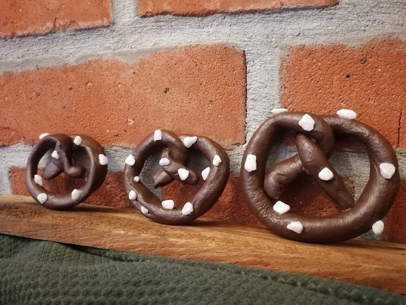 May include: Three chocolate pretzel shaped ornaments with white sprinkles. The ornaments are arranged in a row on a wooden surface.