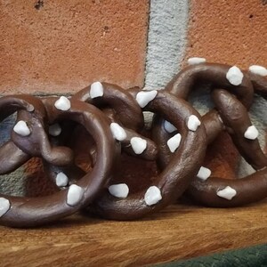 May include: Three brown pretzel shapes with white sprinkles. The pretzels are arranged in a row on a wooden surface.