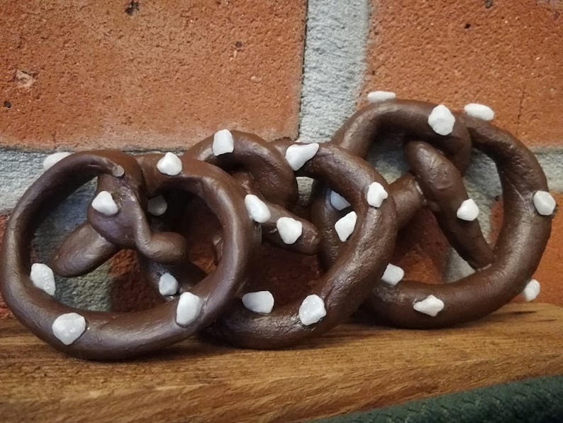 May include: Three brown pretzel shapes with white sprinkles. The pretzels are arranged in a row on a wooden surface.