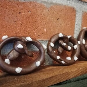 May include: Three brown pretzel shaped ornaments with white icing. The ornaments are arranged in a row on a wooden surface.
