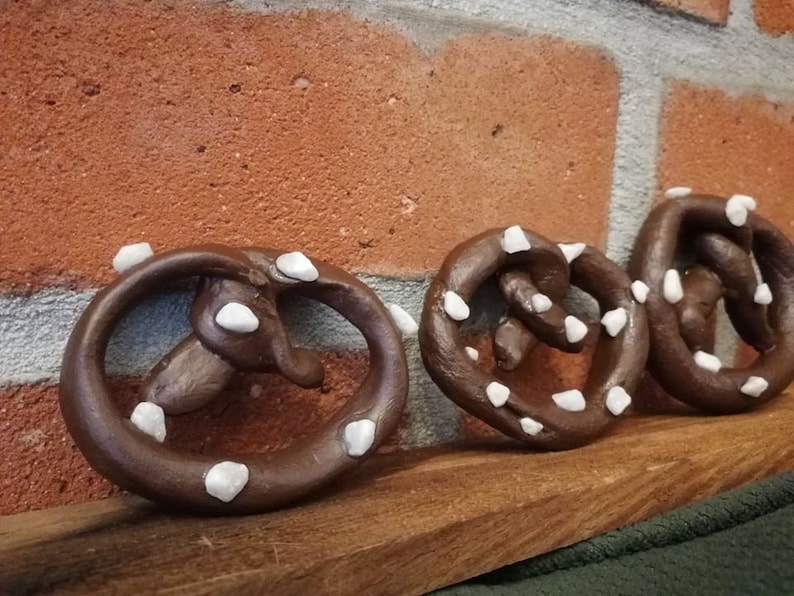 May include: Three brown pretzel shaped ornaments with white icing. The ornaments are arranged in a row on a wooden surface.