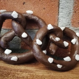 May include: Two brown pretzel shaped ornaments with white sugar crystals on a wooden surface.