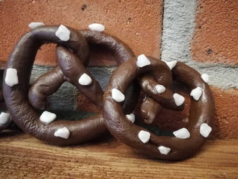 May include: Two brown pretzel shaped ornaments with white sugar crystals on a wooden surface.