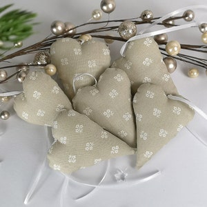 Könnte beinhalten: Sechs beigefarbene Stoffherzen mit weißen Blumenmustern und weißen Schleifen.
