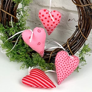 Könnte beinhalten: Vier rosa Stoffherzen mit verschiedenen Mustern, die an einem braunen Zweigkranz hängen. Die Herzen haben Punkte, Wirbel und Streifen.