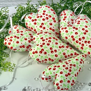 Könnte beinhalten: Fünf rote und grüne herzförmige Kissen mit einem Kirsch- und Blattmotiv. Die Kissen sind aus Stoff und haben einen weißen Hintergrund.