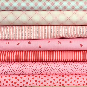 Könnte beinhalten: Stapel von rosa und rotem Stoff mit verschiedenen Mustern, darunter Gingham, Punkte, Streifen und Wirbel.