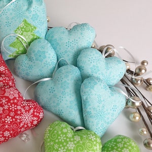 Könnte beinhalten: Eine Sammlung handgemachter herzförmiger Ornamente mit einem Schneeflockenmuster. Die Ornamente sind aus blauem und grünem Stoff gefertigt und eignen sich perfekt zum Dekorieren eines Weihnachtsbaums oder zum Hinzufügen einer festlichen Note zu Ihrem Zuhause.