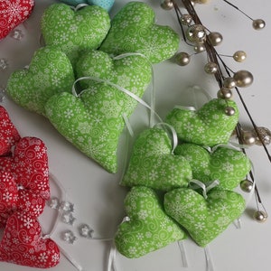 Könnte beinhalten: Eine Sammlung grüner Filzherzen mit einem weißen Schneeflocken- und Wirbelmuster. Die Herzen sind mit weißem Band aneinandergereiht.