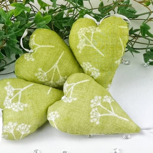 Könnte beinhalten: Vier grüne Stoffherzen mit weißem Blumenmuster. Die Herzen liegen in einer Gruppe auf einer weißen Oberfläche.