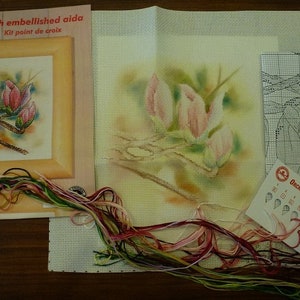 Könnte beinhalten: Ein Kreuzstich-Set mit einem farbenfrohen Blumendesign mit rosa Blüten und grünen Blättern. Das Set enthält einen bedruckten Stoff, Stickgarn und Anleitungen. Das Set ist mit "Orchidéa" beschriftet.
