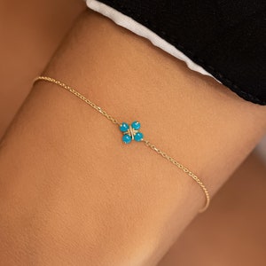 May include: A delicate gold chain bracelet with a small turquoise flower charm.