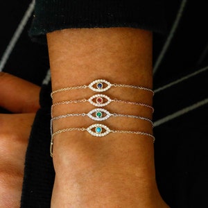 May include: Four gold chain bracelets with a diamond-encrusted evil eye charm. Each charm has a different colored gemstone in the center: blue, red, green, and turquoise.