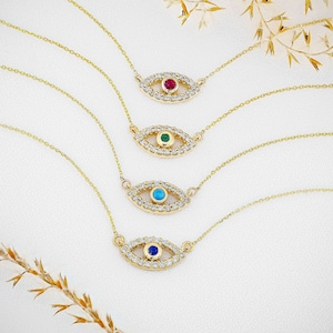 Könnte beinhalten: Vier goldene Halsketten mit einem diamantbesetzten bösen Auge als Anhänger. Jeder Anhänger hat einen andersfarbigen Edelstein in der Mitte: rot, grün, blau und dunkelblau.