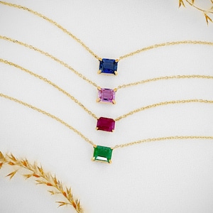 Könnte beinhalten: Vier goldene Halsketten mit verschiedenen Edelsteinen. Die Halsketten zeigen einen blauen Saphir, einen rosa Saphir, einen roten Rubin und einen grünen Smaragd.