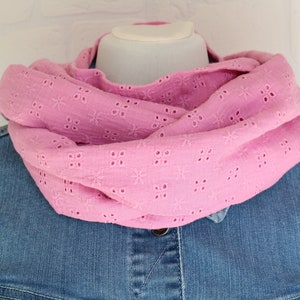 Könnte beinhalten: Ein rosa Lochmuster-Loop-Schal ist über einer Schaufensterpuppe drapiert. Der Schal besteht aus einem weichen, leichten Stoff und hat ein Blumenmuster. Der Schal wird über einer Jeansjacke gezeigt.