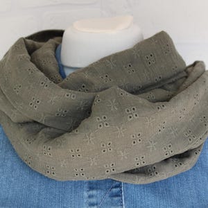Könnte beinhalten: Olivgrüner Loop-Schal aus leichtem Stoff mit floralem Lochmuster. Der Schal ist über einem Schaufensterpuppenkopf und einer Jeansjacke drapiert.