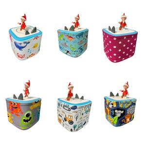 Peut inclure: Six boîtes décoratives avec des motifs variés et une petite figurine sur le dessus. Les boîtes ont différentes housses en tissu avec des motifs comme des dinosaures, des monstres et des créatures marines. Chaque boîte a des accents d'ailerons de requin gris.