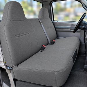 May include: A charcoal gray fabric seat cover set installed on a truck bench seat. The cover features a textured material, integrated headrests, visible seat belt buckles, and a center shoulder strap, providing a fitted look for the vehicle interior.