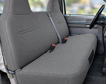 May include: A charcoal gray fabric seat cover set installed on a truck bench seat. The cover features a textured material, integrated headrests, visible seat belt buckles, and a center shoulder strap, providing a fitted look for the vehicle interior.
