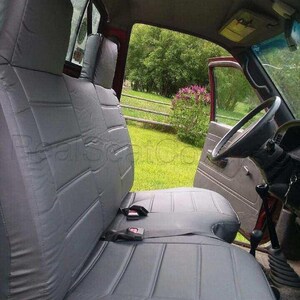 May include: Gray car seat covers with a quilted pattern. The covers are installed in the front seats of a pickup truck. The seats have headrests and seat belts.