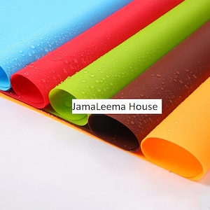 Peut inclure: Gros plan sur plusieurs tapis en silicone enroulés de différentes couleurs : bleu, rouge, vert, marron et jaune. Des gouttelettes d'eau sont visibles sur les surfaces. Le texte "JamaLeema House" est imprimé.