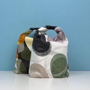 May include: Two reusable lunch bags with a geometric pattern of circles in shades of green, black, white, and beige. The bags have black handles.