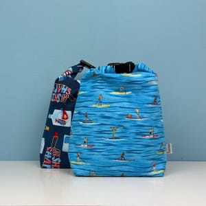 Puede incluir: Dos bolsas de la compra reutilizables. Una es azul con texto blanco que dice "My Ships Sails" y la otra es azul con un patrón de personas haciendo paddle surf en un océano azul.