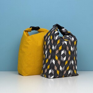 May include: Two fabric lunch bags. One is mustard yellow with white polka dots. The other is black with a geometric pattern of yellow, grey, white, and brown diamonds. Both bags have a black buckle closure at the top.