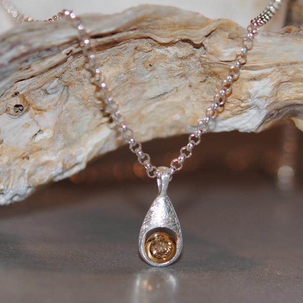 May include: A silver necklace with a teardrop-shaped pendant featuring a small, round, golden gemstone.