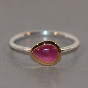 Op de afbeelding: Een zilveren ring met een getextureerde band en een roze edelsteen gezet in een gouden zetting.