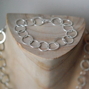 Op de afbeelding: Een zilveren ketting met grote, open, ronde schakels. De ketting wordt getoond op een houten standaard.