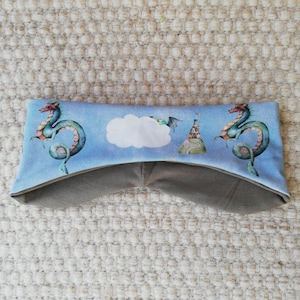 Könnte beinhalten: Ein blaues Stirnband mit einer weißen Wolke und zwei grünen Drachen auf hellblauem Hintergrund. Das Stirnband ist aus weichem, dehnbarem Stoff.