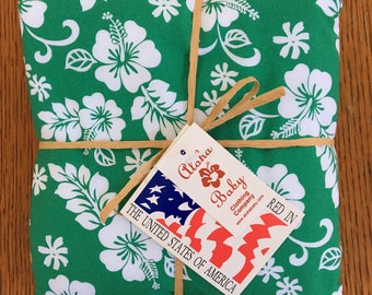May include: A green fabric with white hibiscus flowers wrapped in brown twine and tied with a tag that reads "Aloha Baby Clothing Company www.alohababy.com RED IN THE UNITED STATES OF AMERICA".