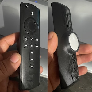 May include: A black remote control with a round directional pad and buttons for volume, play, pause, and other functions. The remote is in a black case with a white button on the top.