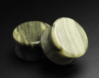 Puede incluir: Dos medidores de oreja de piedra verde y blanca. Los medidores son redondos y tienen un acabado liso y pulido.