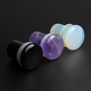 May include: Three ear gauges, one black, one purple amethyst, and one white opal.