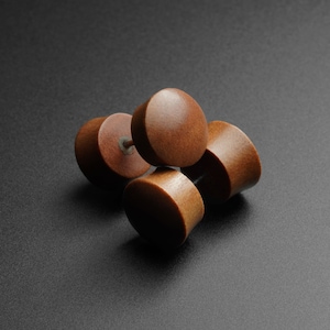 May include: Four brown wooden ear gauges of different sizes, stacked on top of each other.
