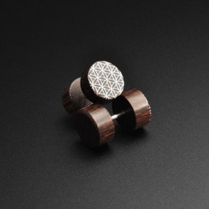 May include: Three wooden ear gauges with a geometric pattern on one side. The gauges are dark brown and have a silver metal post.