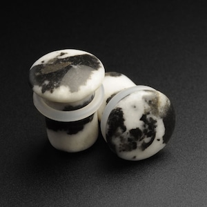May include: Two black and white marble plugs for stretched earlobes. The plugs are round and have a smooth, polished surface.