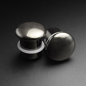 May include: Two black metal ear gauges, one with a white ring around the base. The gauges are smooth and shiny.