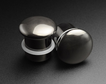 May include: Two black metal ear gauges, one with a white ring around the base. The gauges are smooth and shiny.