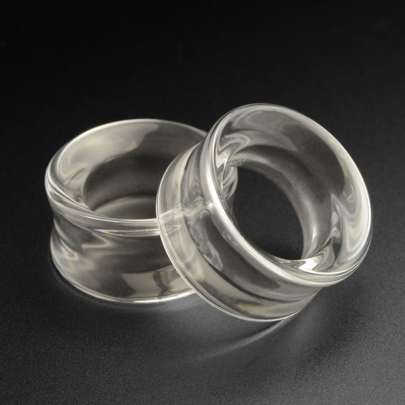 May include: Two clear acrylic ear gauges, one larger than the other, on a black background.