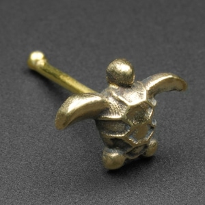 May include: A gold-colored nose ring with a detailed turtle design. The turtle is facing forward with its head raised and its wings outstretched.
