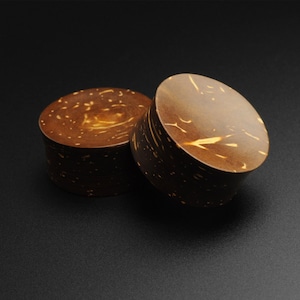 May include: Two brown wooden ear gauges with a natural wood grain pattern. The gauges are round and have a smooth finish.