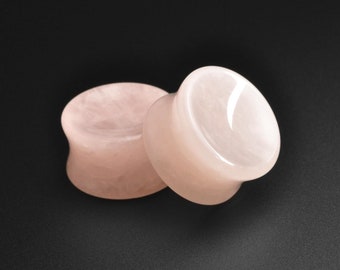 May include: Two pink rose quartz ear gauges, one slightly larger than the other, on a black background.