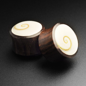 Könnte beinhalten: Ein Paar Holzohrstecker mit einer weißen Muscheleinlage mit einem Spiralmuster. Die Stecker sind dunkelbraun mit einer natürlichen Holzmaserung.