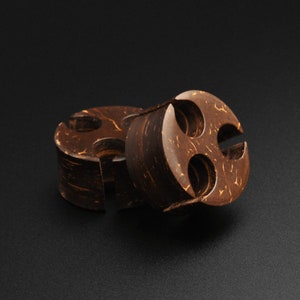 Puede incluir: Molinillo de madera de coco marrón oscuro de dos piezas con un diseño único. El molinillo tiene forma circular con una superficie texturizada y un patrón distintivo de cortes. Las piezas están separadas.
